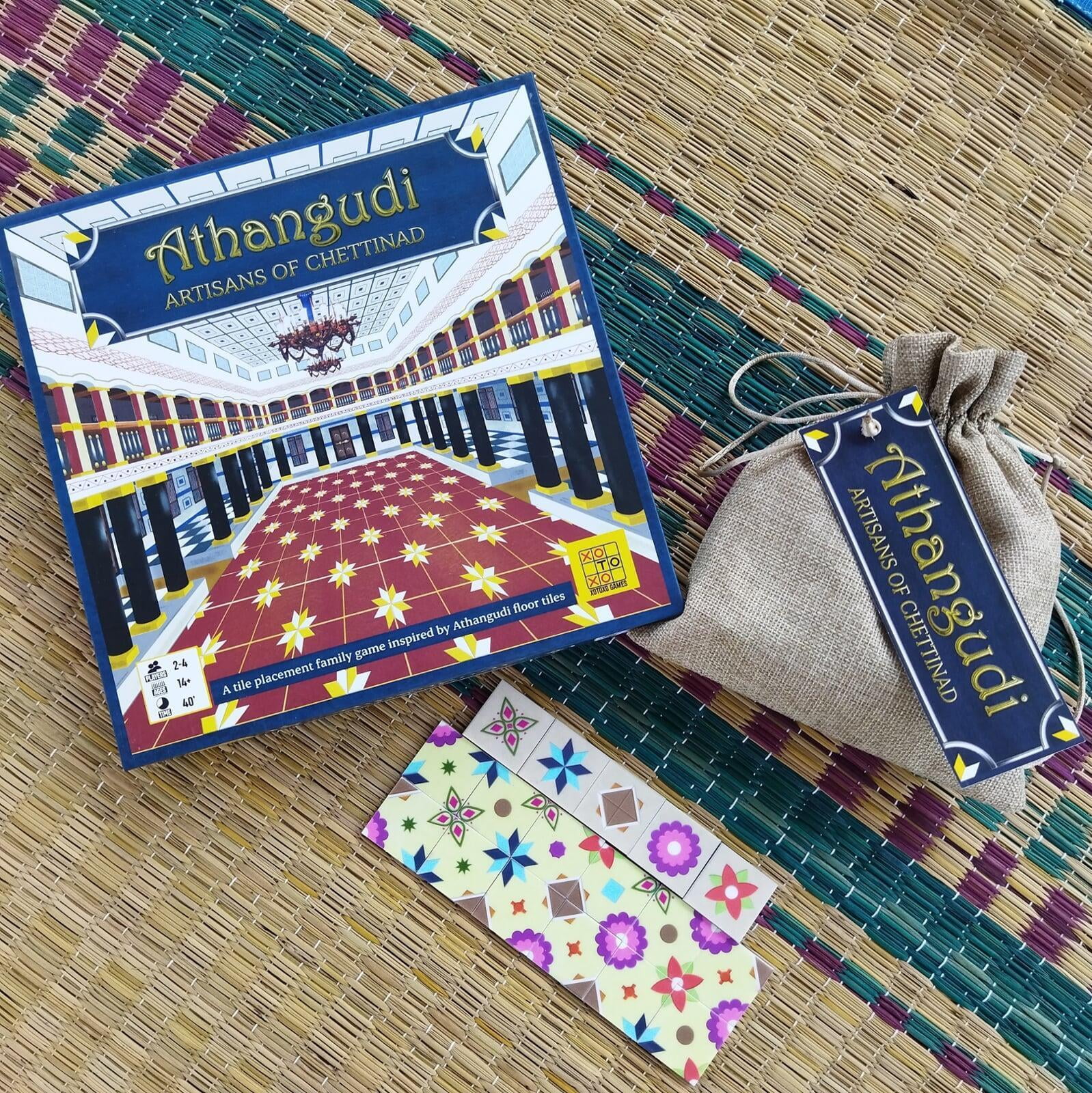Boardgame named Athangudi: Artisans of Chettinad, placed next to a jute pouch, and some tiles from the game, on a straw mat