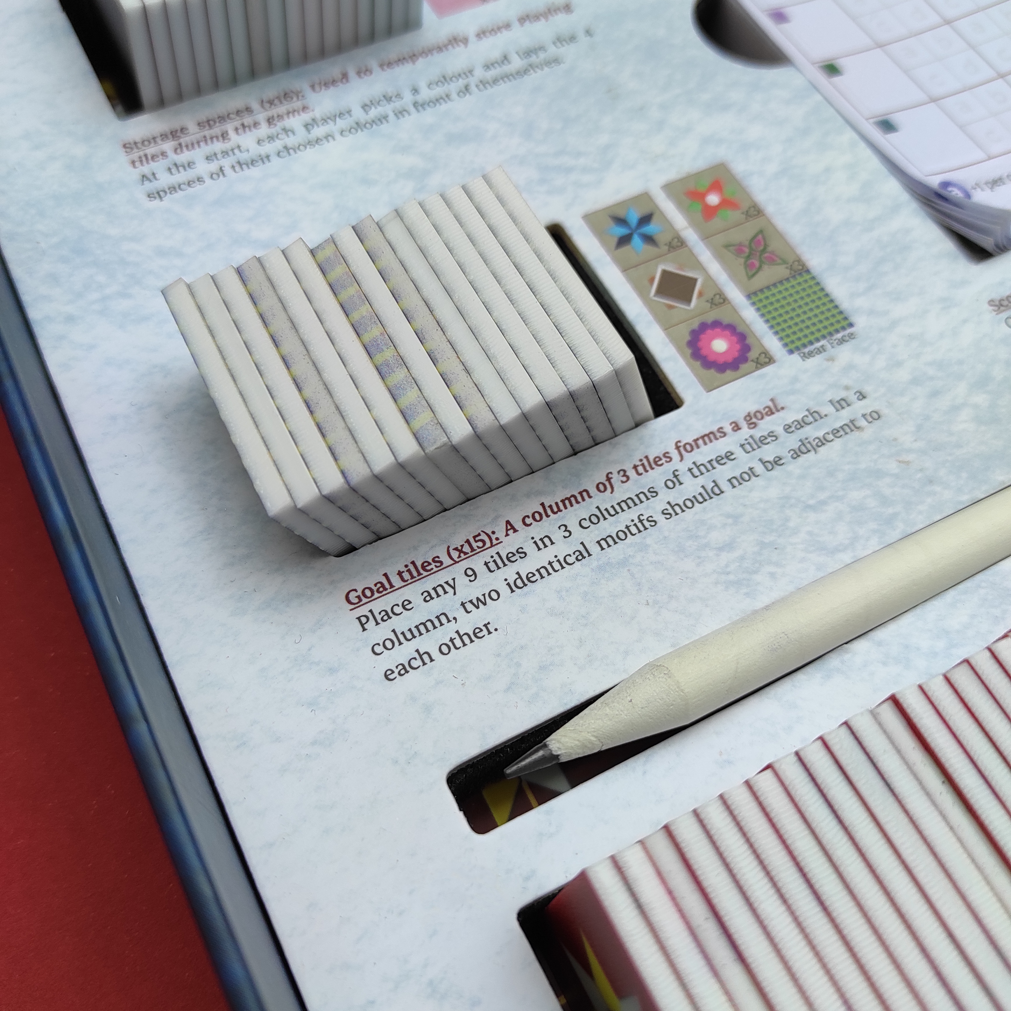 Close up image of "Rulebox" of the boardgame Athangudi: Artisans of Chettinad. The image is a close up of the interior insert of the game box. Instructions on how to set up game components are visible on the inside of the box, next to the components. 